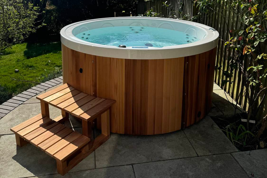 Round wooden hot tub with steps in a garden setting
