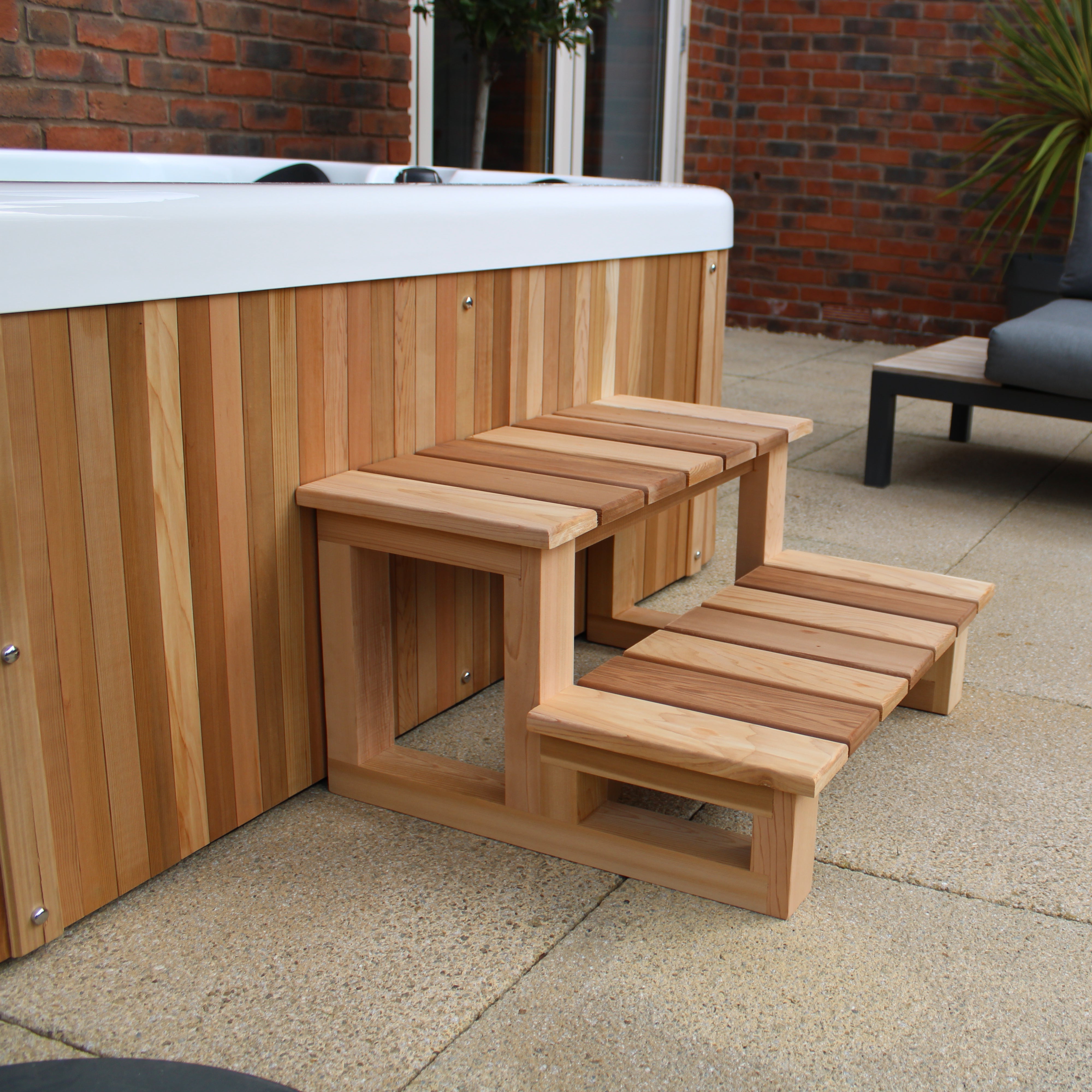 Wooden steps leading to a hot tub with a gray sofa in the background.